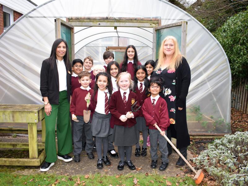 Oak Cottage Primary School's Eco-committee outside their polytunnel, with Let's Go Zero Climate Action Advisor Kumari Kher (left) and the school's sustainability lead Jane Newman (right)